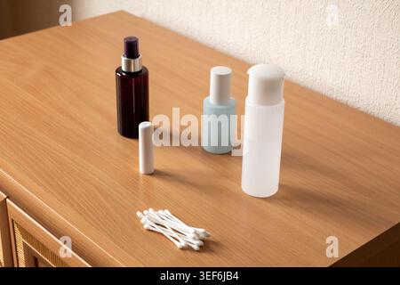 Cosmetic bottles and cotton swab on wooden table for beauty product advertisement. Minimalist essential personal care items. Stock Photo