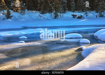 Frozen River Sunrise with Snow Covered Rocks and Pine Forest Winter Landscape Stock Photo