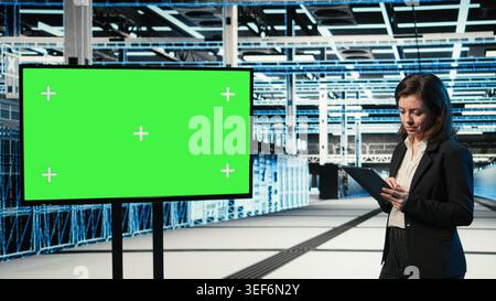 Chroma key monitor used by woman in data center to monitor industrial automation systems. Female admin in server room uses isolated screen display to oversee equipment performance Stock Photo