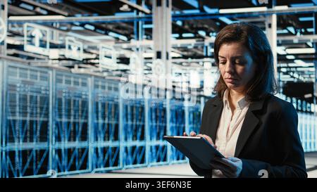 Data center software developer coding on tablet, scanning rigs to create augmented reality digital twin. Woman in server farm running programming script on device, VFX overlay Stock Photo