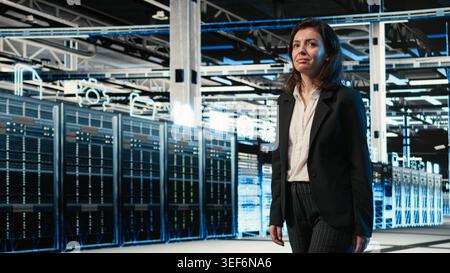 Smiling manager inspecting futuristic data center with blue wireframe mesh overlay. Happy IT professional walking through server room rows visualizing digital twin data streams Stock Photo
