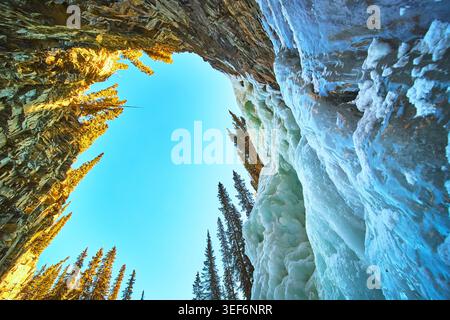 Frozen Waterfall and Rocky Cliffs with Pine Trees in Winter Forest Landscape Stock Photo