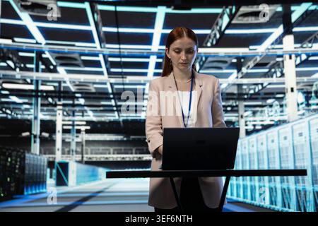 Data center software developer using laptop program to evaluate equipment diagnostic reports. Server hub expert scripting automated workflows using notebook application to oversee mainframes Stock Photo