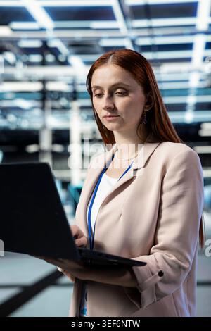 Data center female engineer using laptop to install and upgrade server racks systems. Server farm specialist using automation software on notebook to monitor IT infrastructure performance Stock Photo