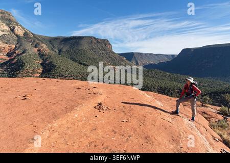 woman hiking onto the deck of Steamboat Rock near Sedona Arizona with Oak Creek Canyon in the background Stock Photo
