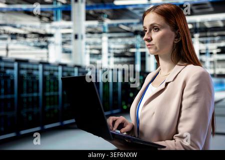 Identifying bottlenecks, laptop and engineer in data center monitoring system performance. Implementing optimizations, notebook and worker in server room improving operational efficiency Stock Photo