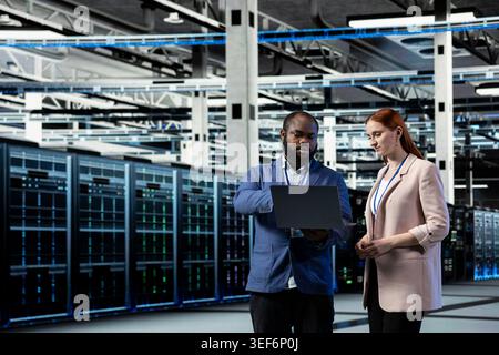 Brainstorming, infrastructure systems and engineering team in data center, managing uptime and efficiency. Upgrade enterprise networks hardware, device and teamworking colleagues in server room Stock Photo