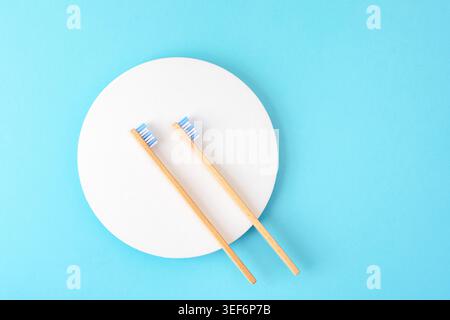 Bamboo toothbrushes on white circle over blue background. Top view, flat lay, copy space. Stock Photo