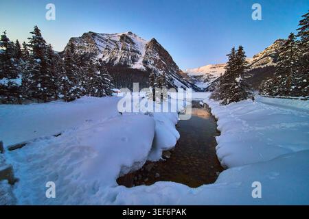 Snow Covered River Evergreens and Mountain Peaks in Winter Landscape Stock Photo