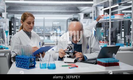 Team of cytotechnologist analyzing bacterial culture slide to test antibiotic efficacy. Biochemists using microscopic gear, observing reaction under lens to develop new medical treatments, camera B Stock Photo