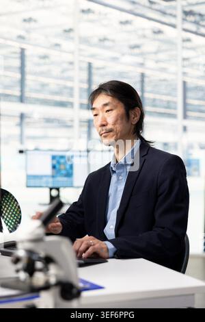 Designing microchip layout, semiconductor manufacturing and senior hardware developer using PC in research facility. Optimizing PCB network topology, computer and elderly Asian man at office desk Stock Photo