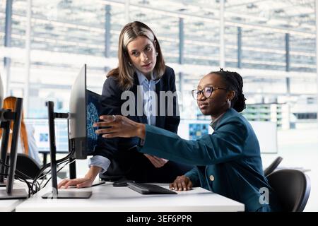 Multiracial QC engineers brainstorming in microchip RD facility, using AI deep learning to upgrade microelectronics. Teamworking colleagues use artificial intelligence to improve semiconductors tech Stock Photo