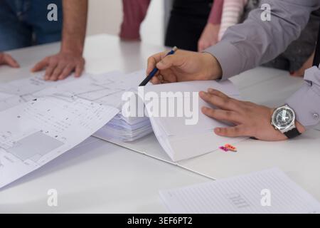 A detailed shot focusing on the hands of an engineer or architect using a pen to point at specific details in a thick binder of technical project docu Stock Photo