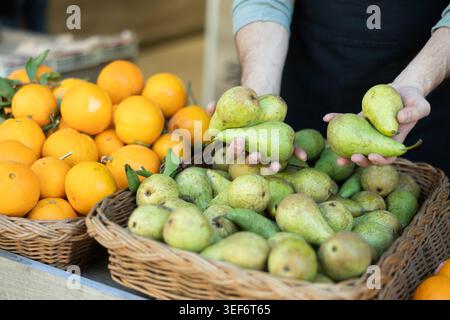 Male seller's hands placing pears on store counter Stock Photo