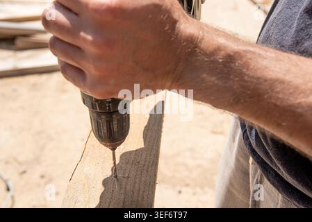 Man Builder Carpenter pilot hole Using Cordless Drill In Wooden Bar Board On sawhorse Stock Photo