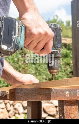Man Builder Carpenter through drilling Using Cordless Drill In Wooden Bar Board On sawhorse Stock Photo