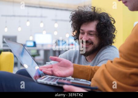 A candid close-up of a young man with a beard and curly hair laughing while looking at a laptop screen. The image captures a positive and high-energy Stock Photo