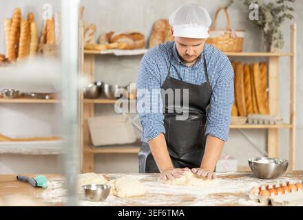 Male baker prepares raw dough, kneads it with his hands Stock Photo