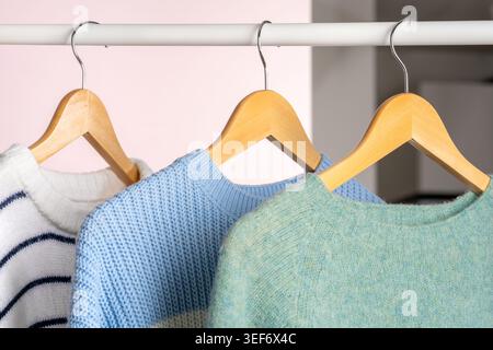Close up woolen knitted sweaters hanging on beige wooden hangers on white clothing rack on store background. Concept of seasonal winter clothing sale, Stock Photo