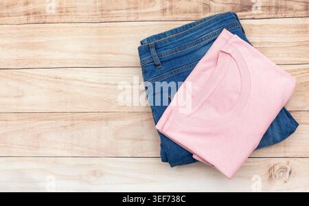 A neatly folded pink T-shirt stacked on blue jeans sits on a warm wooden background. The soft fabric contrasts with the denim texture, creating a clea Stock Photo