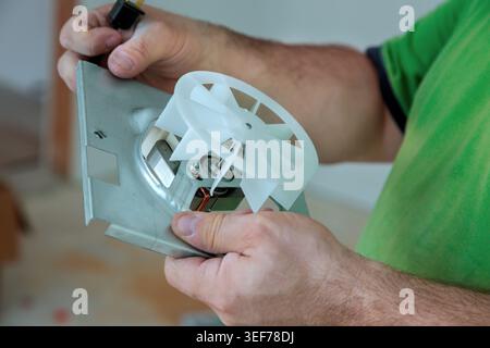Contractor holds cooling fan while repairing mechanical device in workshop Stock Photo