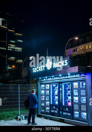 Man standing in front of illuminated Secret Packs vending machines in Berlin Friedrichshain at night, Germany. Mystery-Box machine, editorial. Stock Photo