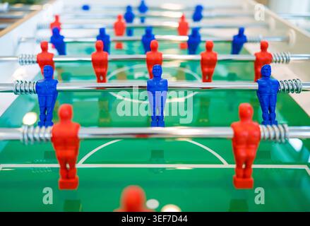 Plastic blue and red team figures stand ready for an indoor sports match on the green field of a recreational foosball table. The popular tabletop game. Stock Photo