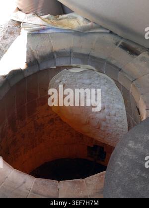 Authentic documentary detail of traditional flatbread baking inside a heated circular brick and clay oven. The dough is stuck directly to the hot maso Stock Photo
