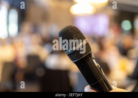 A close-up cropped view of a speaker holding a wireless microphone during a presentation at a corporate seminar or business conference. Stock Photo