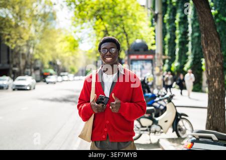 Cheerful black male with positive expression waiting for public transport and smiling at camera. Stock Photo