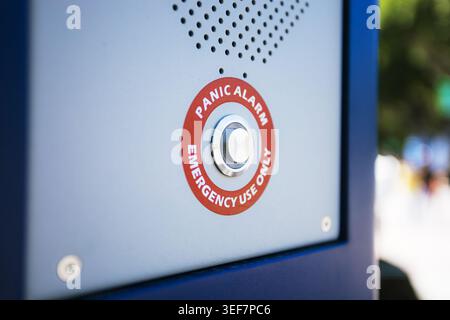Close-up detail of a metallic emergency button with a red circular warning label on a blue pillar. Stock Photo