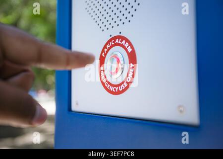 Close-up of a finger about to press a metallic panic button with a red warning label on an urban pillar. Stock Photo