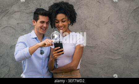 Young multicultural couple using smartphone to watch online content. Concept of streaming, entertainment and digital lifestyle. Stock Photo