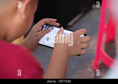 Boy sitting playing game on smartphone, online interaction in real world setting, modern digital behavior, close up. Stock Photo