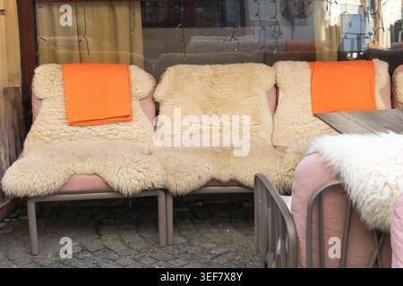 Cozy outdoor cafe seating featuring pink chairs draped with cream sheepskin rugs and bright orange blankets in Bucharest. Stock Photo