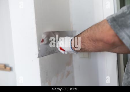 Performing wall repair using a stainless steel trowel to apply finishing material. The technician works in a well lit space, ensuring a smooth application on the surface. Stock Photo