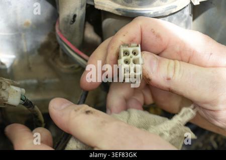 Close-up of dirty mechanic hands connecting electrical plug connector during ATV quad bike engine wiring repair, vehicle maintenance concept Stock Photo