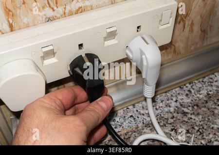 A man's hand inserts a plug into a socket. Sockets in the wall, wires in the socket on the kitchen wall, overloaded wall sockets, home fire safety con Stock Photo