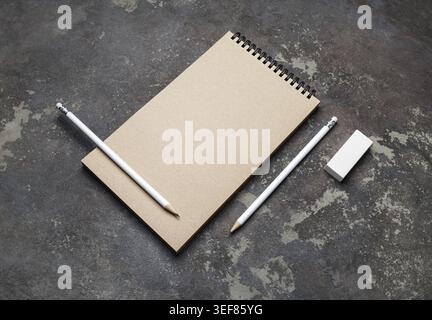Photo of closed blank kraft sketchbook, pencils and eraser on concrete background. Stationery template Stock Photo