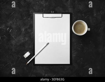 Photo of clipboard with blank letterhead, coffee cup, pencil and eraser on black plaster background. Blank stationery template. Flat lay Stock Photo