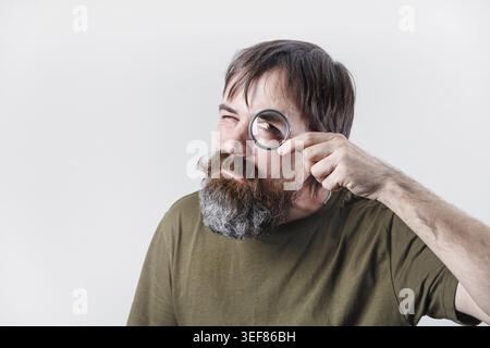 Curious bearded man see through magnifying glass. Science and curiosity concept Stock Photo