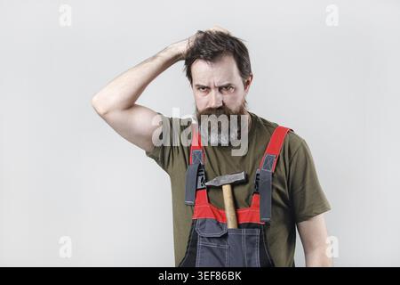 Thoughtful worker in overalls with a hammer in his pocket Stock Photo