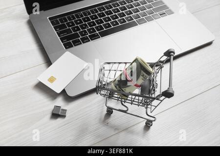 Online shopping concept. Laptop, shopping trolley, credit card, money and usb flash drive on light wooden background Stock Photo