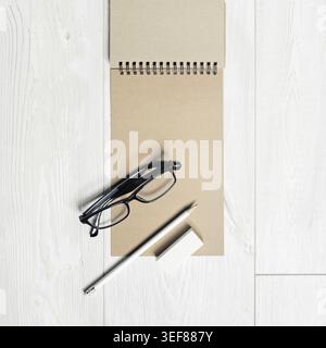 Photo of blank kraft notepad, pencil, eraser and glasses on light wooden background. Responsive design mockup Stock Photo