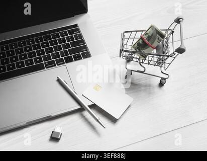 Online internet shopping concept. Laptop, shopping trolley with money, credit card, pen and flash drive Stock Photo