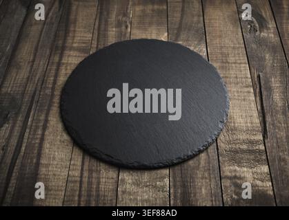 Blank black round slate plate on wooden surface. Copy space Stock Photo