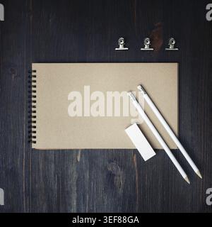 Photo of closed blank kraft sketchbook, pencils and eraser on wood table background. Template for placing your design. Flat lay Stock Photo