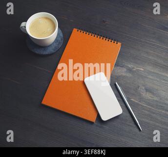 Blank business template. Blank orange notebook, smartphone, coffee cup and pen on wood table background Stock Photo