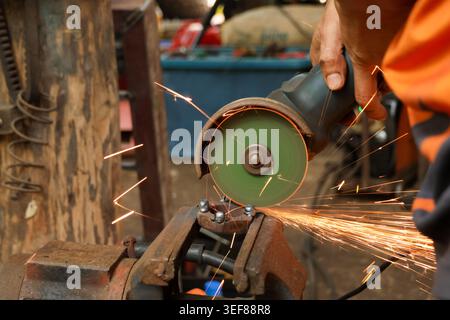 Worker operating angle grinder on metal piece creating bright sparks in workshop environment with focused attention on industrial task building mechan Stock Photo