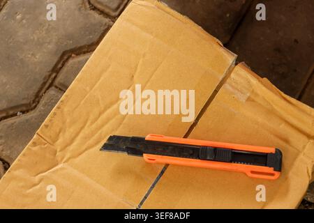 Bright orange utility knife resting on sealed brown cardboard box packaging ready for opening with feeling of eager anticipation for new delivery on s Stock Photo